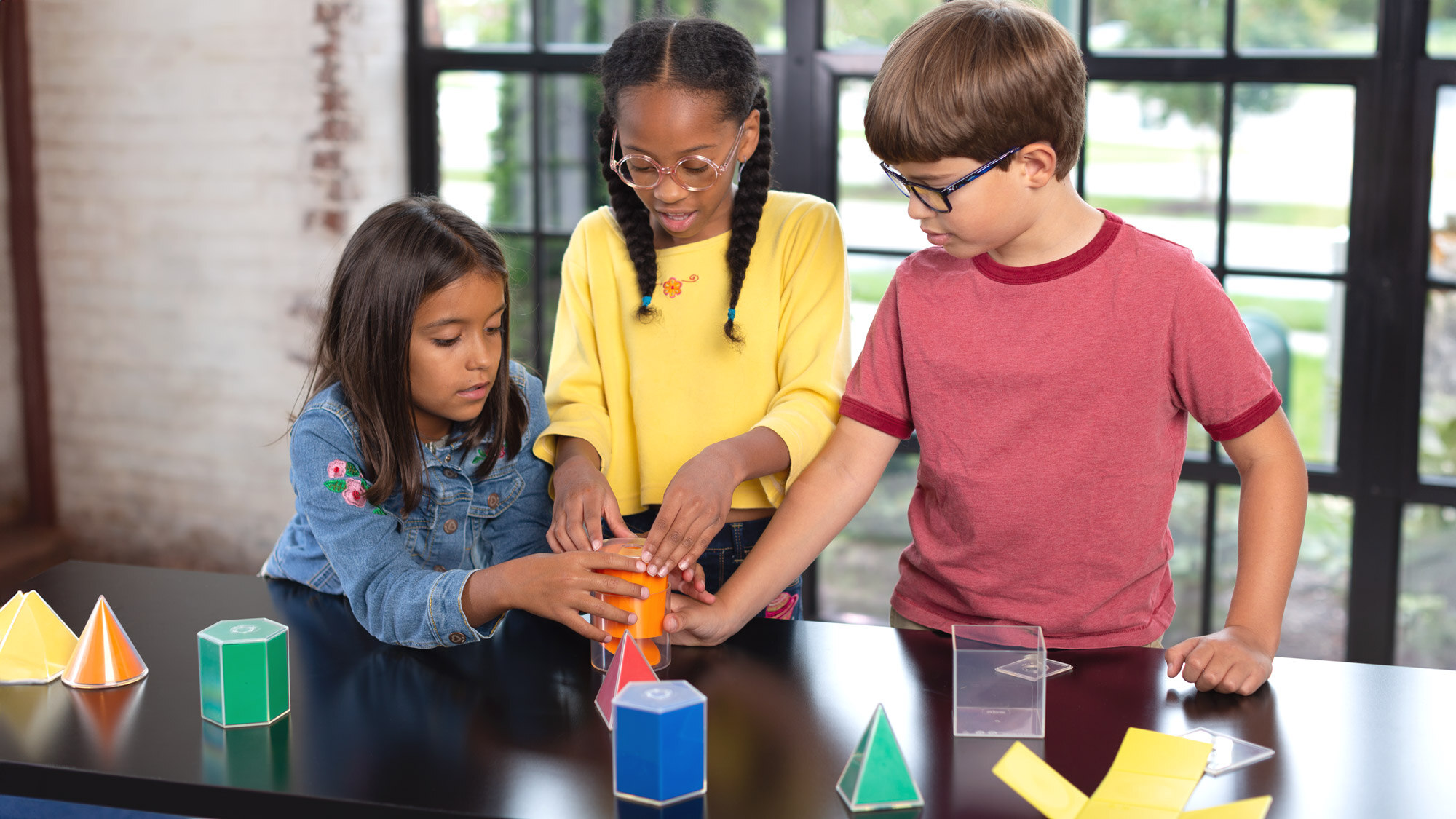 Three students at a table work to build 3-d shapes.